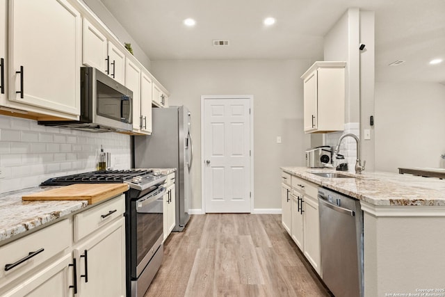 kitchen with appliances with stainless steel finishes, a sink, light wood-style flooring, decorative backsplash, and visible vents