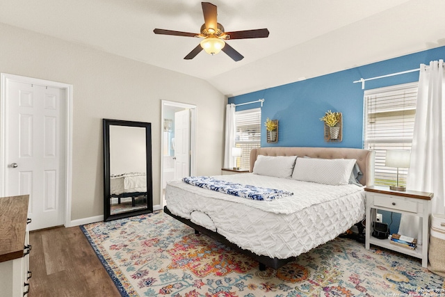 bedroom with a ceiling fan, baseboards, wood finished floors, ensuite bathroom, and vaulted ceiling