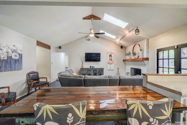 living area with vaulted ceiling with skylight, a brick fireplace, rail lighting, a ceiling fan, and visible vents