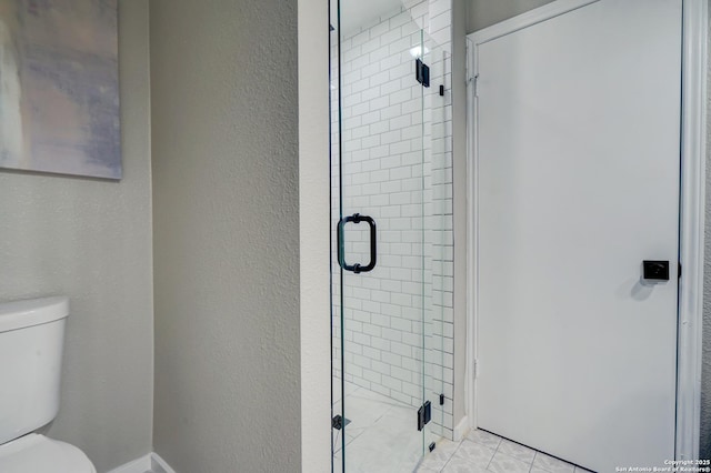 bathroom with a textured wall, tile patterned floors, toilet, and a shower stall
