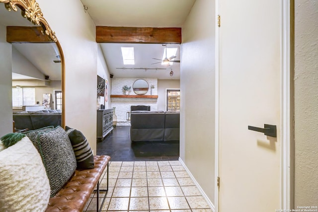 kitchen featuring a skylight, a brick fireplace, beam ceiling, baseboards, and open floor plan