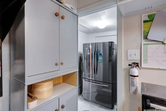 kitchen with light countertops, freestanding refrigerator, a textured ceiling, and white cabinetry