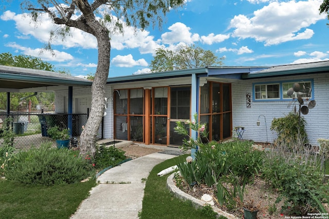 view of front facade featuring a sunroom, fence, and brick siding