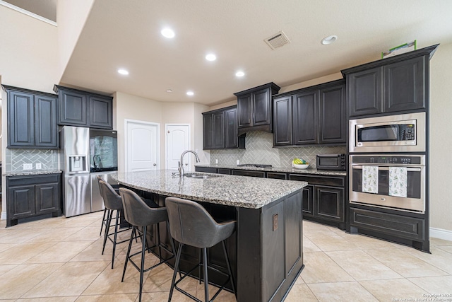 kitchen featuring visible vents, light stone countertops, a sink, backsplash, and stainless steel appliances