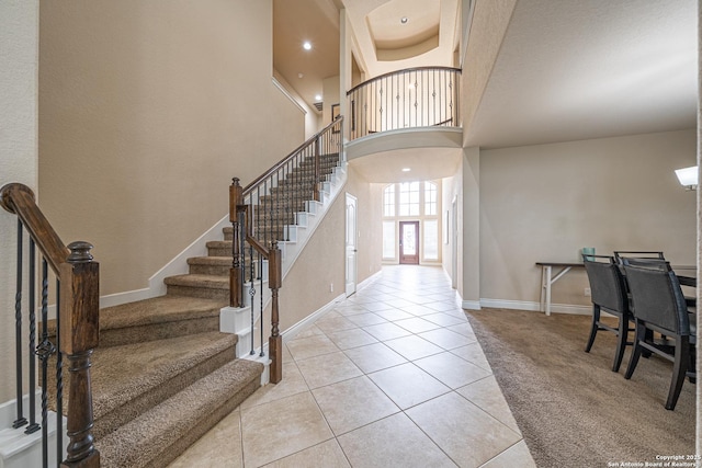 foyer entrance with light carpet, baseboards, a high ceiling, stairway, and light tile patterned floors