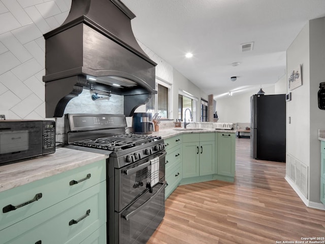 kitchen with visible vents, green cabinetry, tasteful backsplash, a sink, and black appliances
