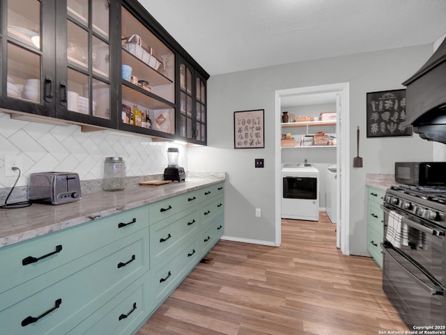 kitchen featuring light stone countertops, light wood-style flooring, tasteful backsplash, washer and clothes dryer, and black appliances