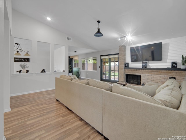 living area with visible vents, a fireplace, vaulted ceiling, baseboards, and light wood finished floors