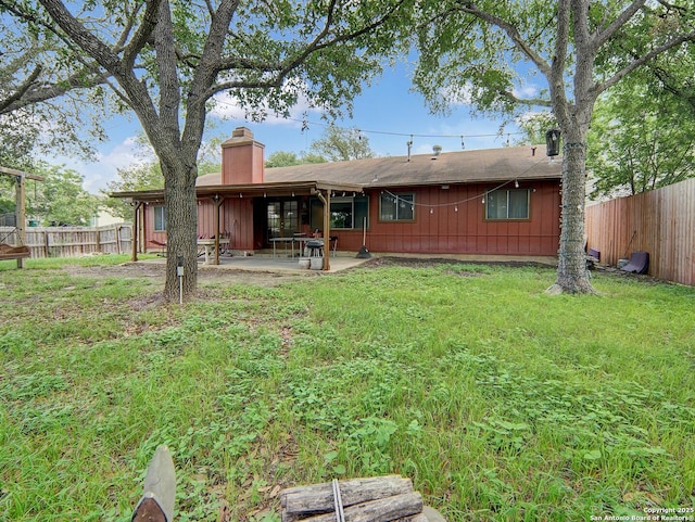 rear view of property with a patio, a lawn, fence, and a chimney