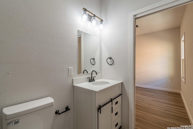 bathroom with a textured wall, vanity, toilet, baseboards, and wood finished floors