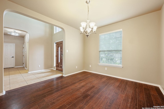 spare room featuring an inviting chandelier, arched walkways, baseboards, and wood finished floors