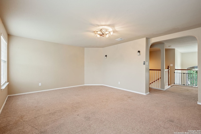 empty room with arched walkways, baseboards, visible vents, and light carpet