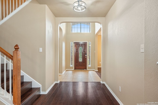 entrance foyer with arched walkways, baseboards, stairs, and wood finished floors