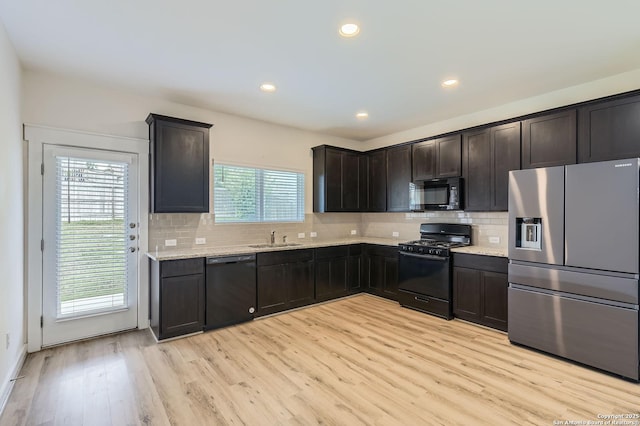 kitchen with tasteful backsplash, a sink, black appliances, and light wood-type flooring