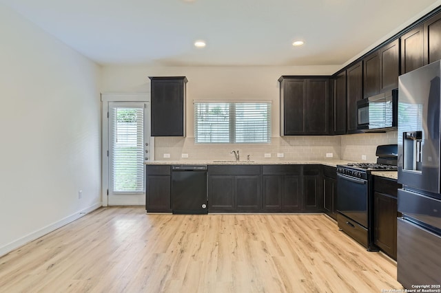 kitchen with a sink, decorative backsplash, black appliances, and light wood finished floors