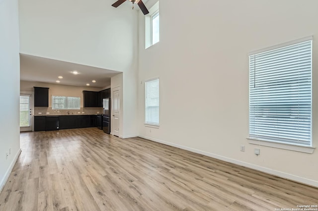 unfurnished living room featuring baseboards, ceiling fan, a high ceiling, recessed lighting, and light wood finished floors