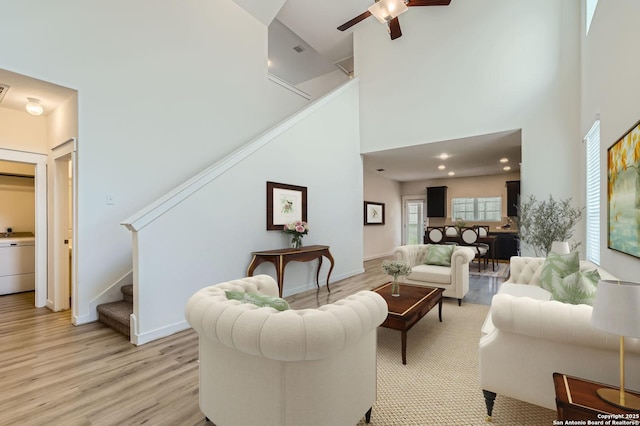 living room featuring light wood-style floors, a ceiling fan, stairs, and a towering ceiling
