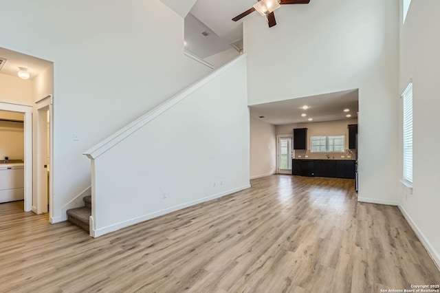 unfurnished living room featuring a ceiling fan, light wood finished floors, a high ceiling, and stairway