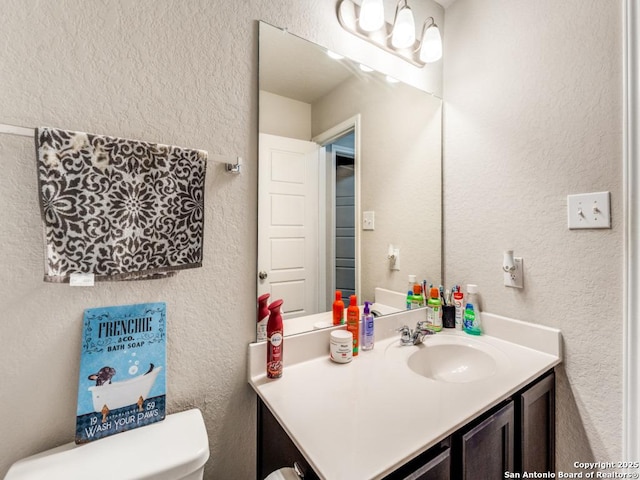 half bath featuring vanity, a textured wall, and toilet