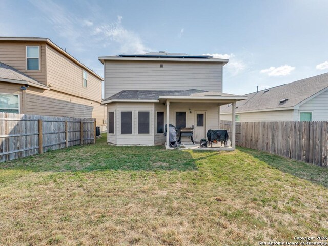 back of property with roof mounted solar panels, a patio, a yard, and a fenced backyard