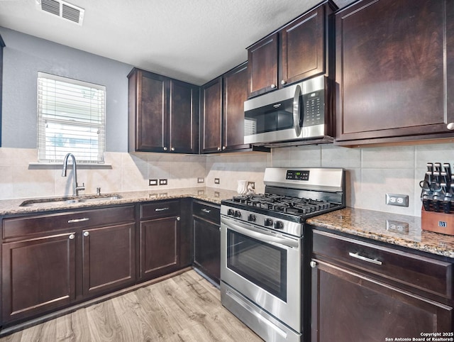 kitchen featuring light stone countertops, appliances with stainless steel finishes, a sink, light wood-style floors, and visible vents