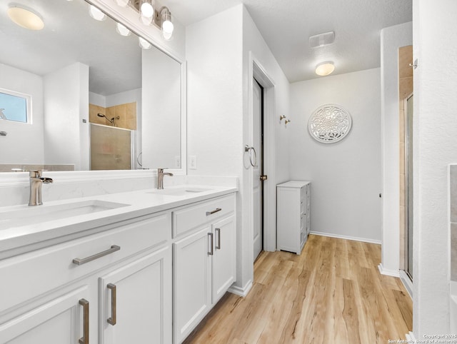 bathroom featuring a sink, double vanity, a stall shower, and wood finished floors