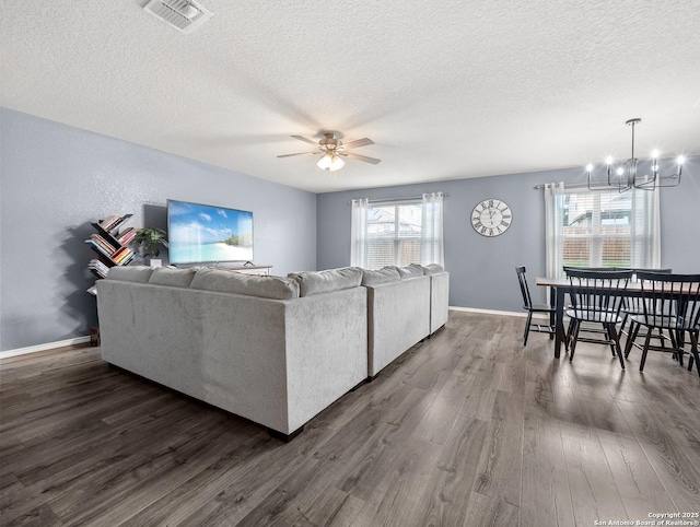 living area featuring visible vents, baseboards, dark wood-type flooring, a textured ceiling, and ceiling fan with notable chandelier