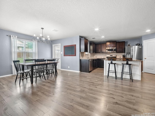 dining space with a textured ceiling, an inviting chandelier, baseboards, and light wood-style floors