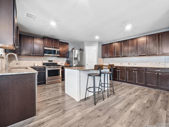 kitchen with a breakfast bar area, visible vents, a sink, light wood finished floors, and stainless steel appliances