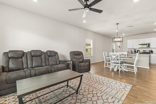 living area with light wood-style flooring, ceiling fan with notable chandelier, recessed lighting, baseboards, and visible vents
