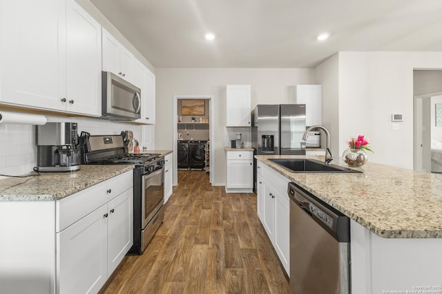 kitchen with appliances with stainless steel finishes, tasteful backsplash, washing machine and dryer, dark wood finished floors, and a sink