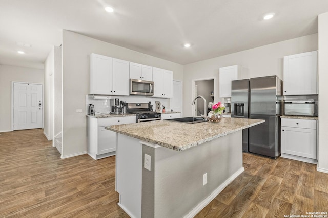 kitchen featuring a sink, a center island with sink, stainless steel appliances, and wood finished floors
