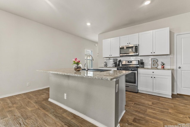 kitchen featuring a center island with sink, light stone counters, a sink, dark wood finished floors, and stainless steel appliances