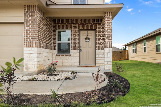 view of exterior entry featuring a lawn, brick siding, fence, an attached garage, and stone siding