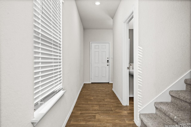 hallway featuring dark wood-type flooring, baseboards, and stairs