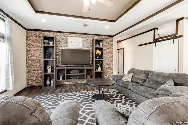 living area with visible vents, crown molding, wood finished floors, a barn door, and a ceiling fan