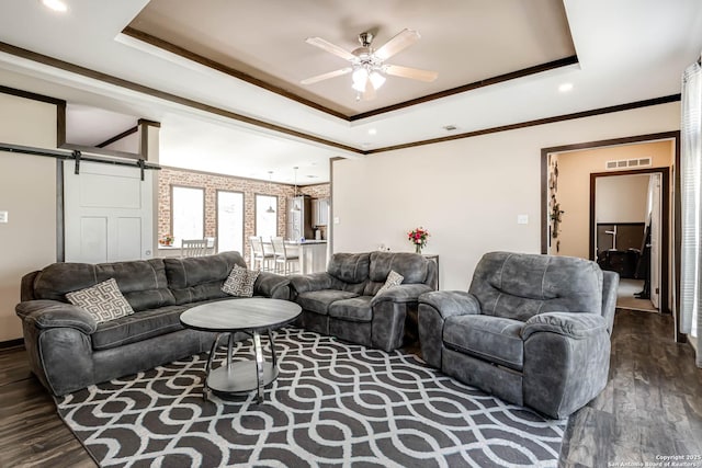 living room with visible vents, ceiling fan, a barn door, a raised ceiling, and dark wood finished floors