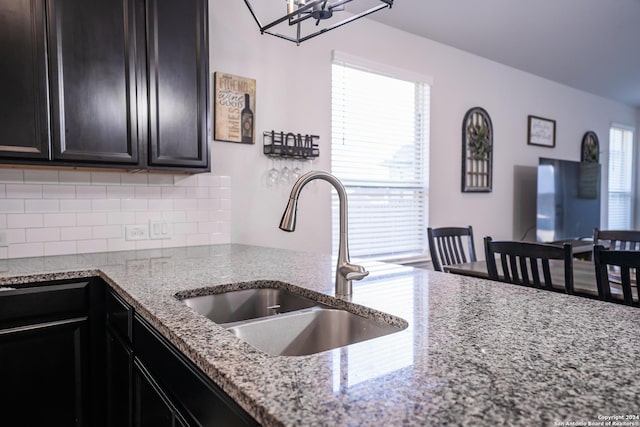 kitchen featuring backsplash, dark cabinets, light stone counters, and a sink