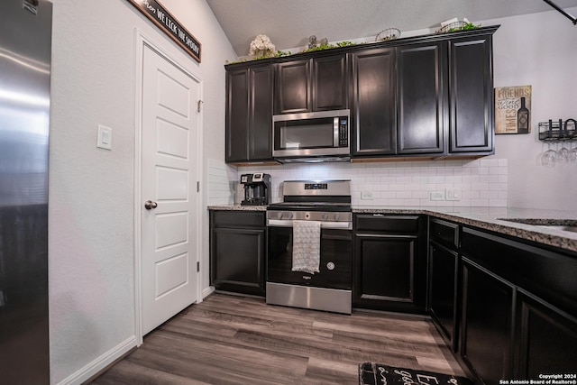 kitchen featuring dark stone counters, stainless steel appliances, dark wood-style flooring, and tasteful backsplash