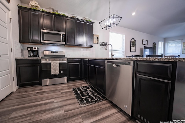 kitchen featuring decorative backsplash, dark wood-type flooring, stone counters, a notable chandelier, and stainless steel appliances