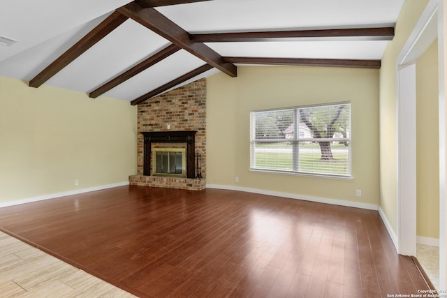 unfurnished living room with baseboards, lofted ceiling with beams, a brick fireplace, and wood finished floors