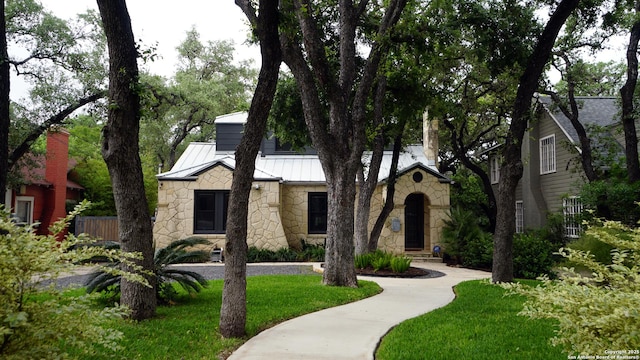 view of front of home featuring fence, a front lawn, stone siding, a standing seam roof, and metal roof