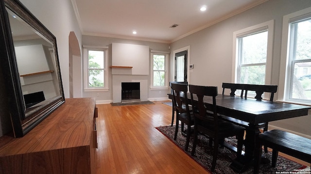 dining room featuring light wood-style floors, a tiled fireplace, recessed lighting, visible vents, and ornamental molding