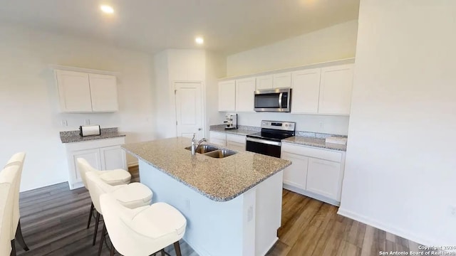 kitchen with wood finished floors, a center island with sink, white cabinets, a sink, and stainless steel appliances