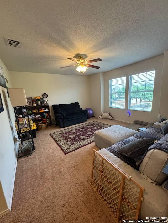 living room with carpet floors, a ceiling fan, a textured ceiling, and visible vents