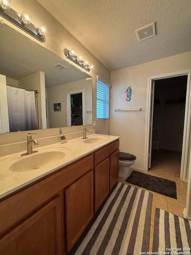 bathroom featuring a sink, double vanity, a textured ceiling, and visible vents