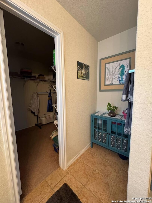 hallway featuring tile patterned flooring, a textured ceiling, and a textured wall