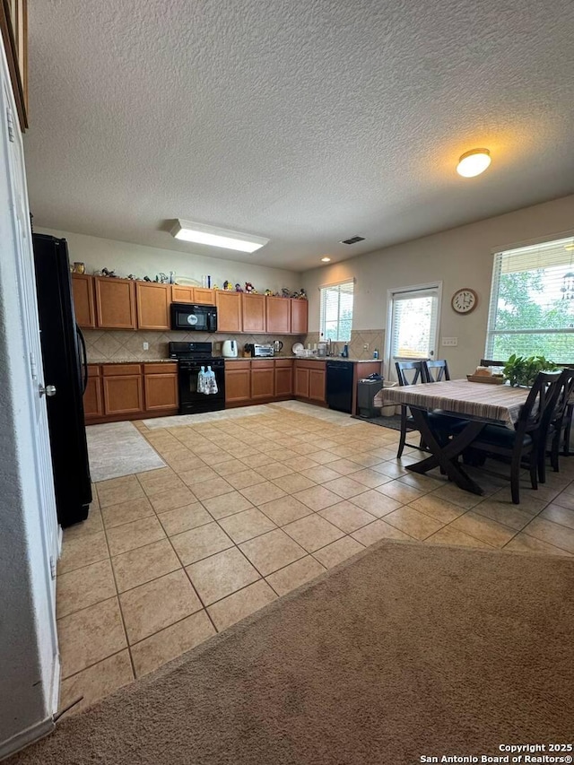 kitchen featuring brown cabinets, light tile patterned flooring, a textured ceiling, backsplash, and black appliances