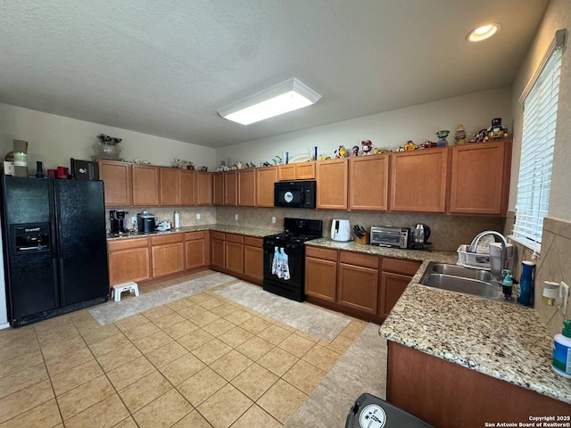 kitchen featuring a sink, brown cabinetry, a toaster, backsplash, and black appliances