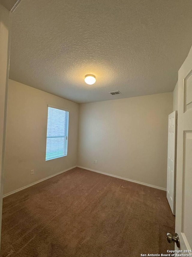 spare room with dark colored carpet, a textured ceiling, baseboards, and visible vents